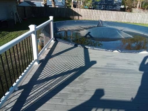 View of a pool cover on a deck with shadows and a fenced yard in the background.
