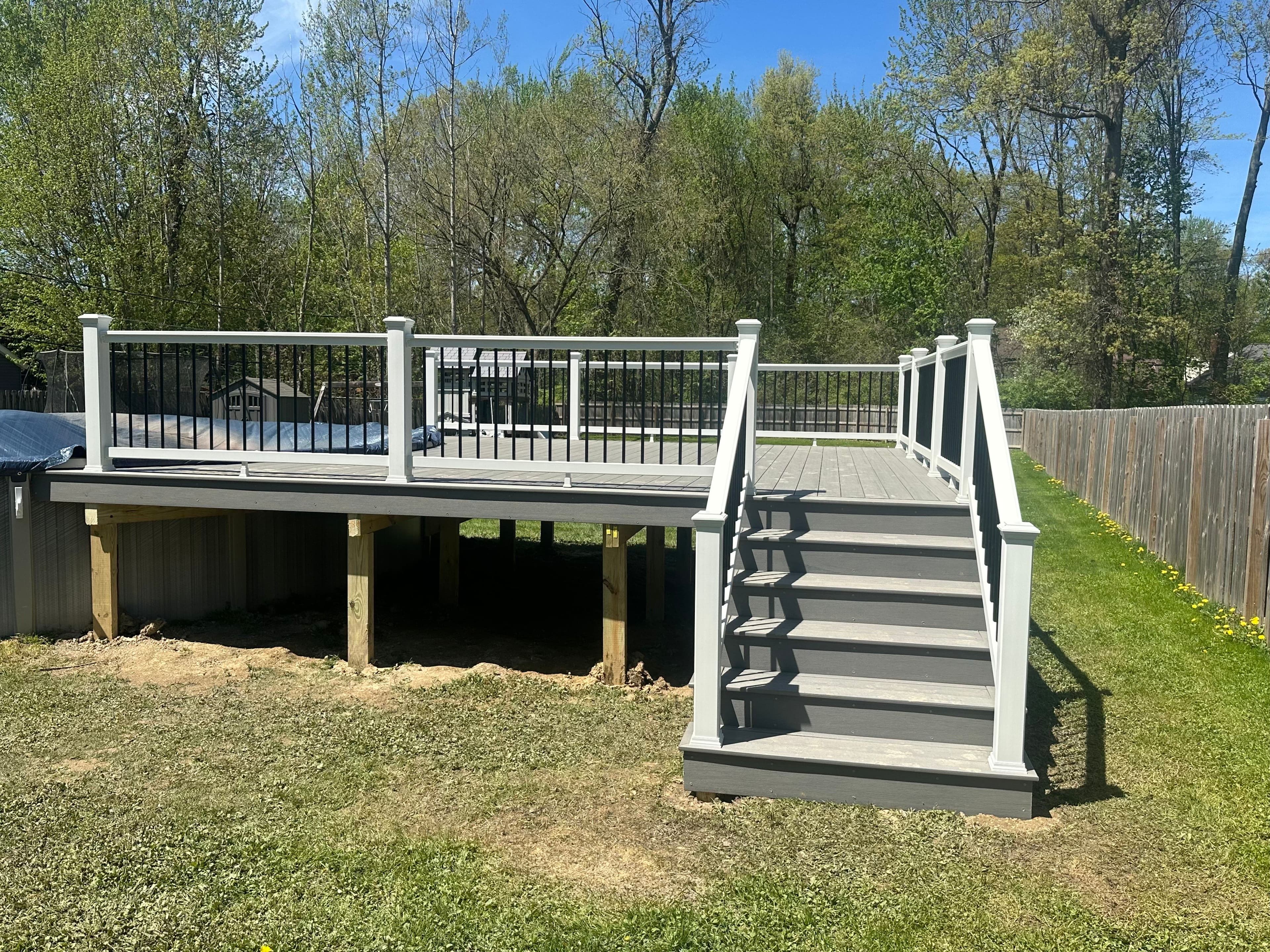 Composite deck with white railings and stairs, surrounded by greenery and trees.
