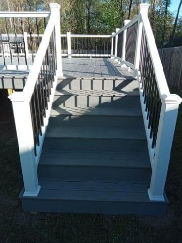 Newly built outdoor staircase with white railings and gray steps, leading to a deck.