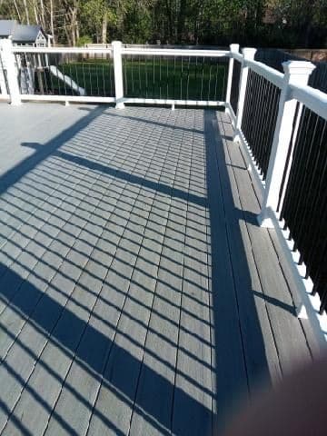 Sunlit deck with railing casting long shadows on gray composite flooring. Ideal outdoor space.