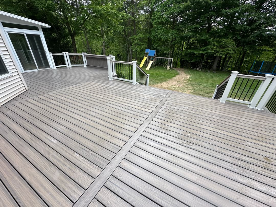 Modern wooden deck with white railings overlooking a grassy yard and play area.