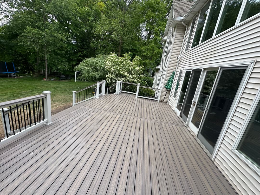 Spacious outdoor deck with railing, surrounded by lush green trees and a yard.